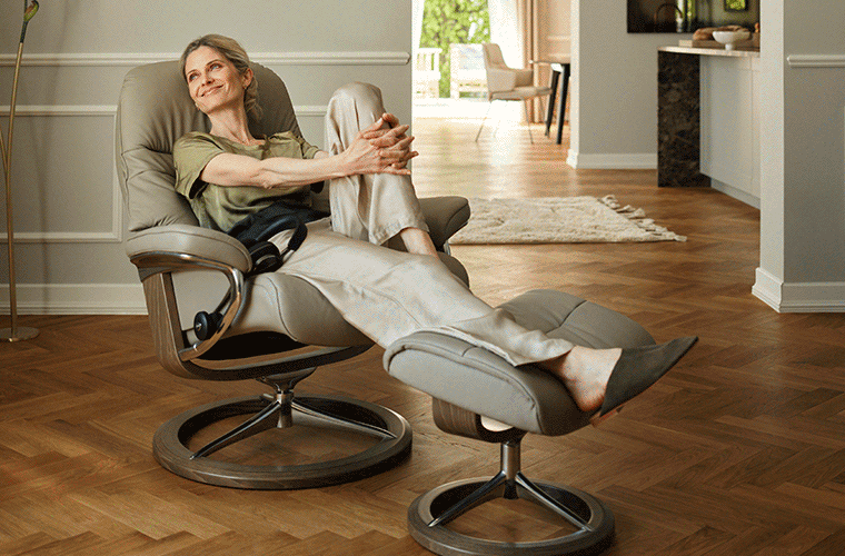 Frau entspannt im beigefarbenen Stressless®-Sessel mit Hocker.