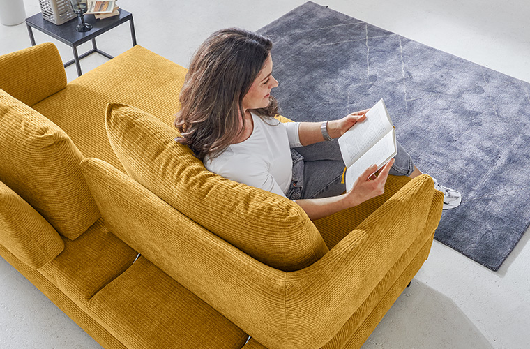 Person sitzt gemütlich auf einem gelben Schlafsofa.