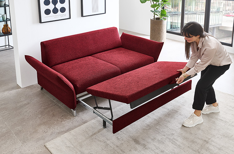 Eine Frau ziehen ein rotes Schlafsofa in einem hellen Raum zu einem Bett aus.
