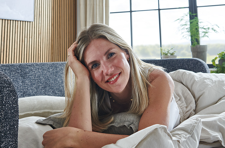 Lächelnde Frau, die auf einem Schlafsofa liegt und in die Kamera blickt.